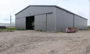 Nowa budowa hali magazynowej w trakcie prac. Widać otwartą bramę, a w tle szare niebo i komin.