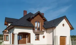 Nowoczesny dom z drewnianymi elementami i czarnym dachem. Wjazd do garażu ozdobiony jest jak cokolik.