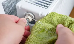 Odkręcanie odpowietrznika, by rozwiązać problem, dlaczego grzejnik jest zimny na dole. Woda kapie na zieloną ściereczkę.