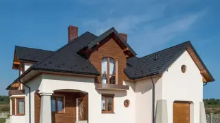 Nowoczesny dom z drewnianymi elementami i czarnym dachem. Wjazd do garażu ozdobiony jest jak cokolik.