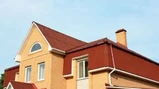 Dom z cegły z czerwonym dachem, okna i komin. Czy to mansarda? Tak, to przestrzeń pod dachem.