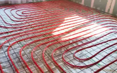 Instalacja ogrzewania podłogowego. Czerwone rurki ułożone na siatce, przygotowane do wylania betonu. To inwestycja, która obniży koszt ogrzewania.