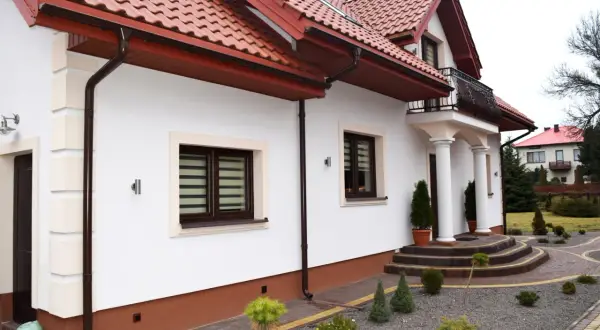 Elegancki cokół na elewacji domu chroni ściany przed wilgocią. Wokół domu zadbany ogród z kamieniami i iglakami.