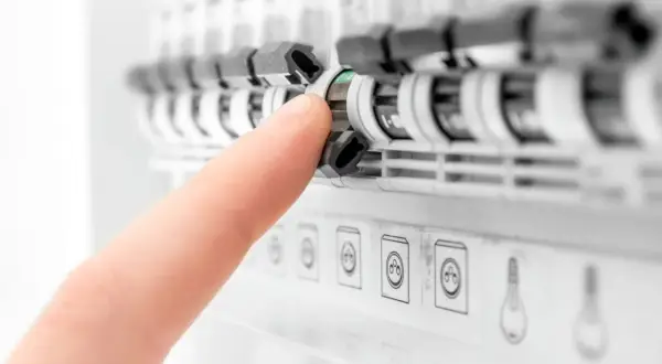 Palec naciska na zielony wskaźnik rozłącznika bezpiecznikowego w tablicy elektrycznej.