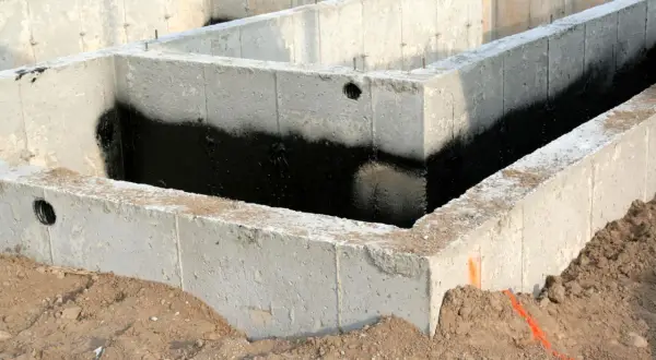 Betonowe bloczki zalewowe tworzą fundament domu, zabezpieczone czarną izolacją przeciwwilgociową.