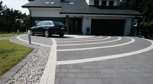 Nowoczesny podjazd z kostki brukowej i żwiru, z eleganckim lany beton na podjazd. Czarny samochód parkuje przed domem.
