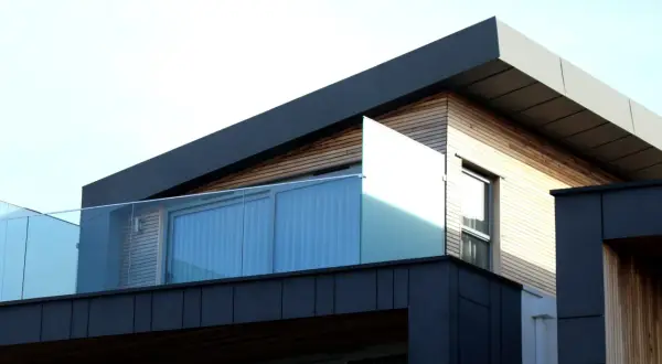 Nowoczesny budynek z drewnianą elewacją i przeszklonym balkonem. Charakterystyczny dach jednospadowy podkreśla geometryczny kształt konstrukcji.