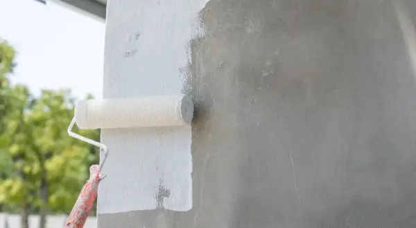 Wałek malarski pokrywa białą farbą szary beton. Prace wykończeniowe na zewnątrz budynku.