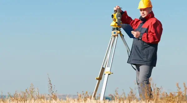 Geodeta w żółtym kasku pracuje z tachimetrem na polu. Zastanawiasz się, ile kosztuje geodeta?