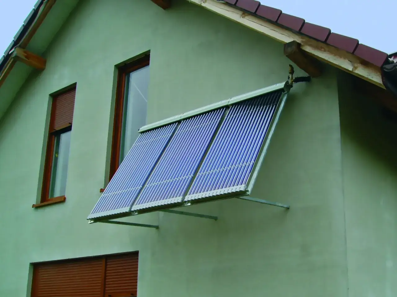 Instalacja solarna na ścianie domu, z rzędami niebieskich rurek, zbiera energię słoneczną.