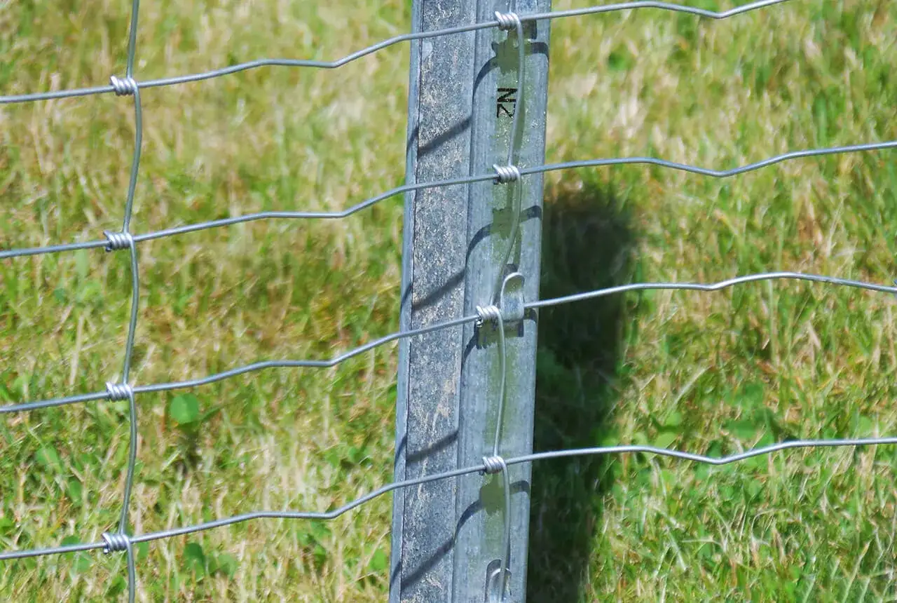 Szczegółowe mocowanie siatki ogrodzeniowej do słupka, z widocznymi drutami i zapięciami.