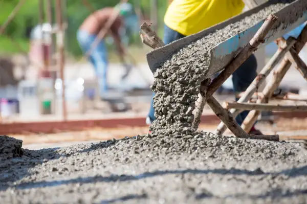 Beton na fundament wylewany z rynny. Pracownicy w tle budują solidną konstrukcję.