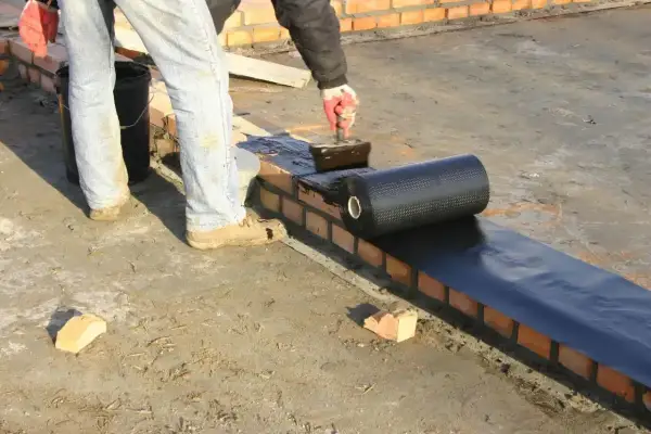 Pracownik kładzie hydroizolację na murze, przygotowując zbrojenie pod dalsze prace budowlane.