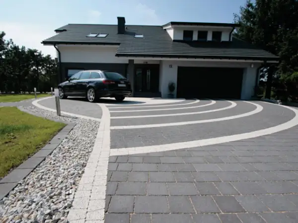 Nowoczesny podjazd z kostki brukowej i żwiru, z eleganckim lany beton na podjazd. Czarny samochód parkuje przed domem.